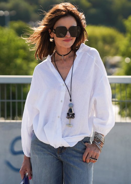 Biała lniana koszula damska oversize z dekoltem V i guzikami, zestawiona z jeansami w lekkiej, miejskiej stylizacji.