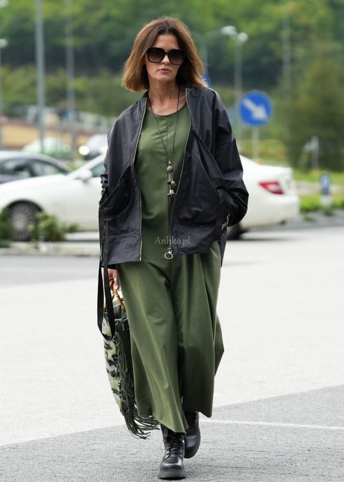Damski kombinezon khaki z szeroką nogawką i długim rękawem, o luźnym kroju, stylizowany z czarnymi botkami i torebką w miejskiej scenerii.