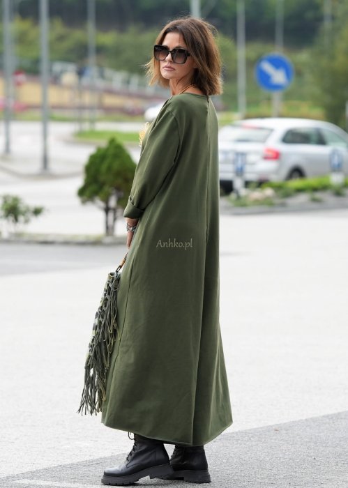 Damski kombinezon khaki z szeroką nogawką i długim rękawem, o luźnym kroju, stylizowany z czarnymi botkami i torebką w miejskiej scenerii.