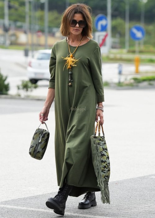 Damski kombinezon khaki z szeroką nogawką i długim rękawem, o luźnym kroju, stylizowany z czarnymi botkami i torebką w miejskiej scenerii.