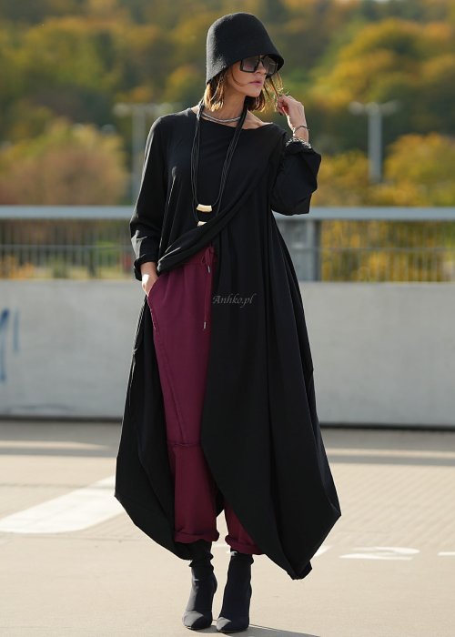 Czarna sukienka maxi o asymetrycznym dole i luźnym kroju oversize. Modelka prezentuje stylizację z czarnymi botkami, kapeluszem i minimalistyczną biżuterią w miejskim stylu.