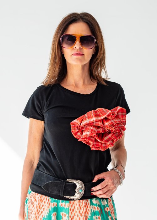 Kobieta prezentuje czarną bluzkę basic z krótkim rękawem i okrągłym dekoltem. Gładki, klasyczny t-shirt zestawiono ze wzorzystą spódnicą i szerokim paskiem w stylu boho.