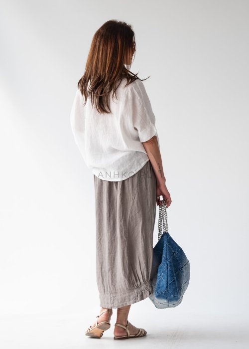Biała koszula lniana oversize z krótkim rękawem i guzikami, stylizowana z luźnymi spodniami w miejskim, minimalistycznym stylu.