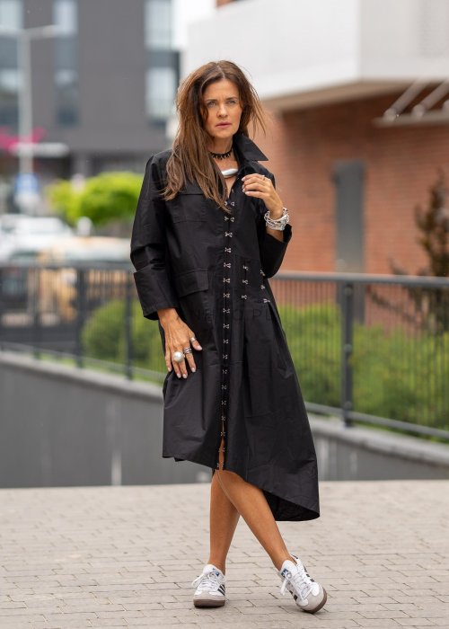 Czarna sukienka koszulowa midi z długim rękawem i ozdobnymi metalowymi zapięciami z przodu. Model pokazany w miejskiej stylizacji ze sneakersami, z wyraźnie zaznaczonym kołnierzykiem i luźnym fasonem.