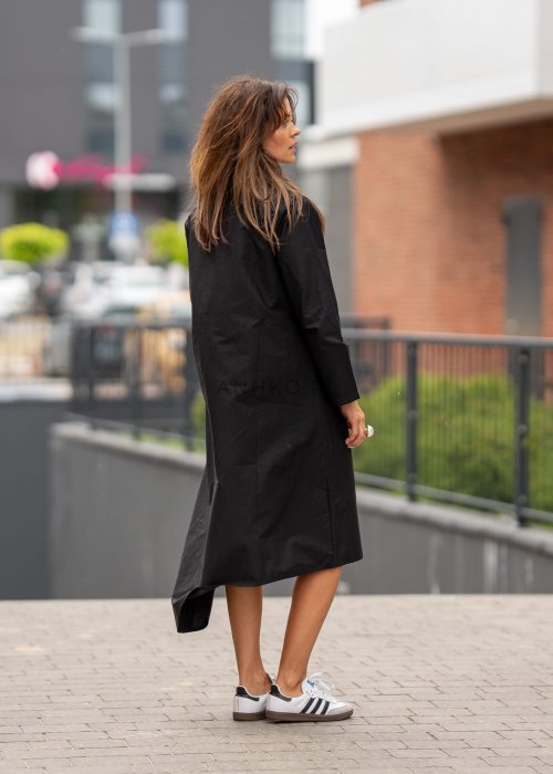 Czarna sukienka koszulowa midi z długim rękawem i ozdobnymi metalowymi zapięciami z przodu. Model pokazany w miejskiej stylizacji ze sneakersami, z wyraźnie zaznaczonym kołnierzykiem i luźnym fasonem.