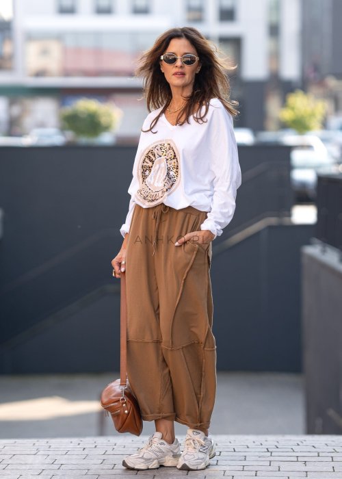Damskie spodnie dresowe w kolorze camel z fantazyjnymi przeszyciami i elastycznym pasem, stylizowane z jasnymi sneakersami w miejskiej scenerii.