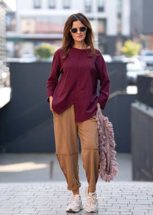 Damskie spodnie dresowe w kolorze camel z fantazyjnymi przeszyciami i elastycznym pasem, stylizowane z jasnymi sneakersami w miejskiej scenerii.