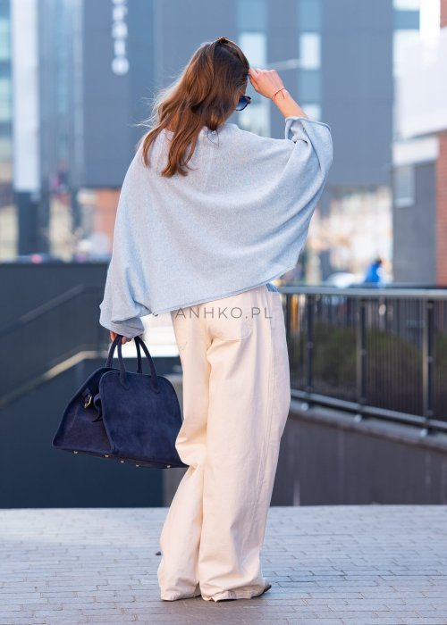 Jasnoniebieski sweter oversize z asymetrycznym dołem, stylizowany z jasnymi szerokimi spodniami i granatową torebką w miejskim looku.