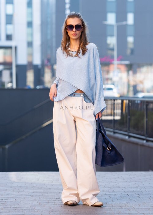Jasnoniebieski sweter oversize z asymetrycznym dołem, stylizowany z jasnymi szerokimi spodniami i granatową torebką w miejskim looku.