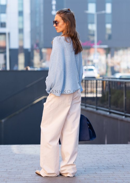 Jasnoniebieski sweter oversize z asymetrycznym dołem, stylizowany z jasnymi szerokimi spodniami i granatową torebką w miejskim looku.