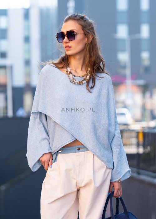 Jasnoniebieski sweter oversize z asymetrycznym dołem, stylizowany z jasnymi szerokimi spodniami i granatową torebką w miejskim looku.
