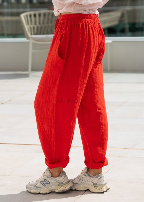 Czerwone lniane spodnie damskie typu baggy z obniżonym krokiem, elastycznym pasem i zwężanymi nogawkami. Komfortowy model zestawiony ze sportowymi sneakersami w codziennej stylizacji.