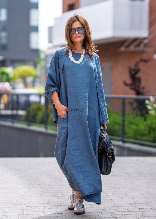 Niebieska sukienka lniana maxi z luźną narzutką, zestawiona z torebką i sneakersami w miejskiej stylizacji.
