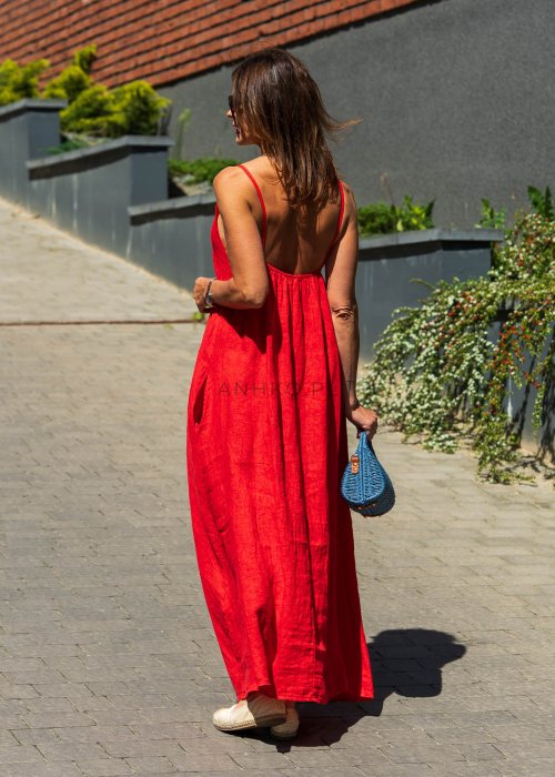 Czerwona lniana sukienka maxi na ramiączkach o luźnym kroju, stylizacja z plecioną torebką i biżuterią w miejskim stylu.