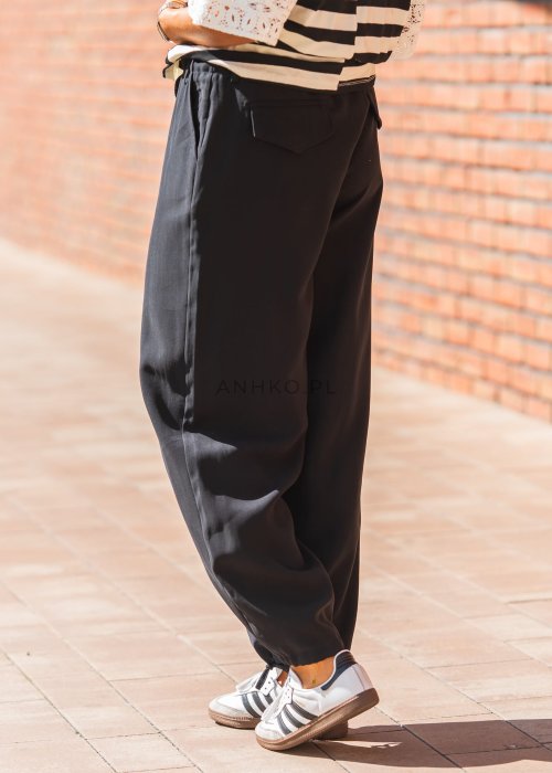 Czarne damskie spodnie z lekkiego materiału, o luźnym kroju z elastyczną talią i ściągaczami przy nogawkach w stylu casual