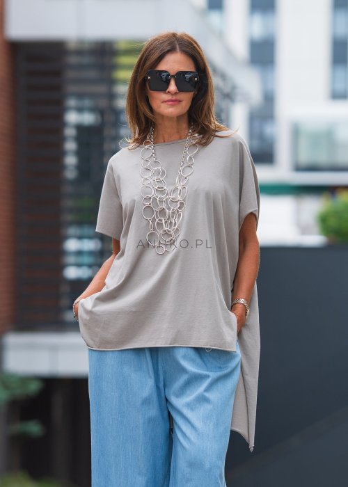 Bluzka oversize taupe z asymetrycznym dołem i wydłużonym tyłem, zestawiona z jasnymi jeansami. Luźny fason tworzy nowoczesną, minimalistyczną stylizację.