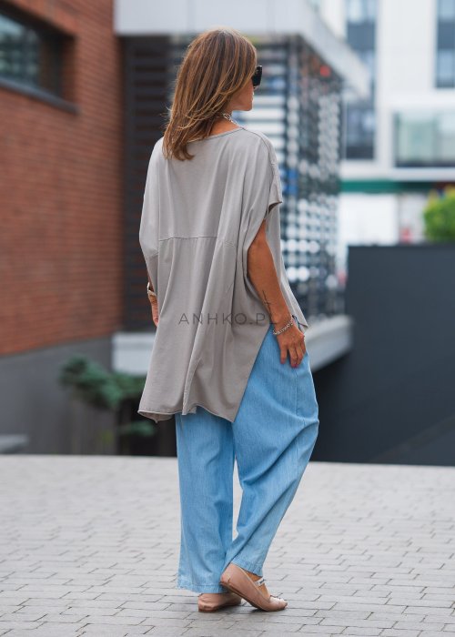 Bluzka oversize taupe z asymetrycznym dołem i wydłużonym tyłem, zestawiona z jasnymi jeansami. Luźny fason tworzy nowoczesną, minimalistyczną stylizację.