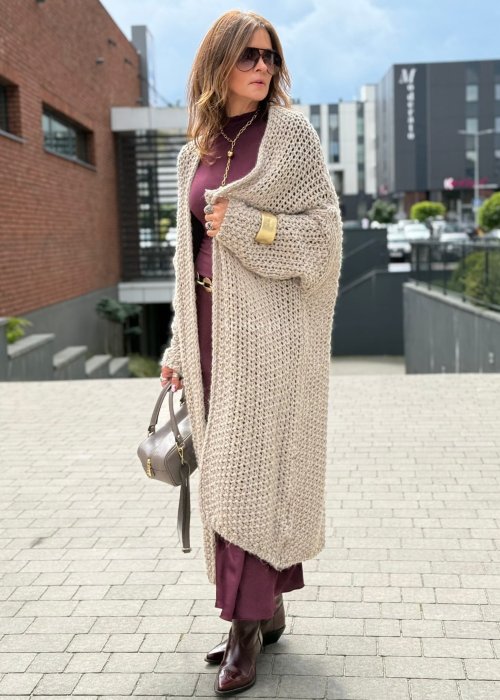 Długi oversize kardigan damski z grubego beżowego splotu, z obniżoną linią ramion, w stylu boho i casualowej mody damskiej