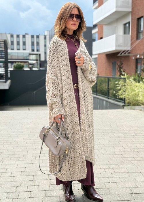 Długi oversize kardigan damski z grubego beżowego splotu, z obniżoną linią ramion, w stylu boho i casualowej mody damskiej