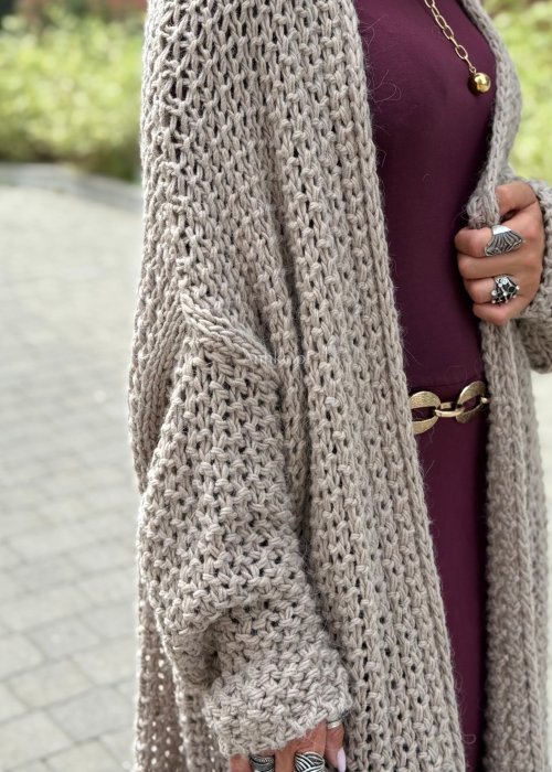 Długi oversize kardigan damski z grubego beżowego splotu, z obniżoną linią ramion, w stylu boho i casualowej mody damskiej