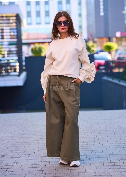 Luźne, szerokie spodnie w kolorze khaki o casualowym charakterze. Model z wysokim stanem, zapinany na duże, ozdobne guziki przesunięte lekko na bok, co nadaje im oryginalności.
