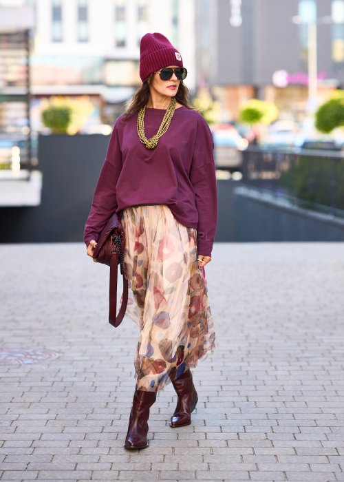 Śliwkowa bluza damska oversize z długim rękawem i naszywką, zestawiona ze wzorzystą spódnicą w stylizacji miejskiej.