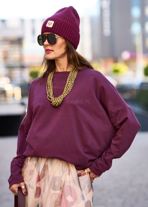 Śliwkowa bluza damska oversize z długim rękawem i naszywką, zestawiona ze wzorzystą spódnicą w stylizacji miejskiej.