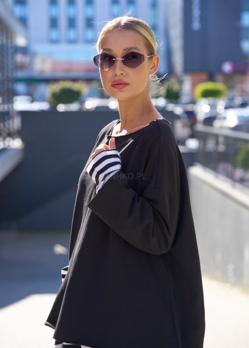 Czarna bluzka oversize z kontrastową kieszenią w biało-czarne paski i długim rękawem, stylizowana z pasiastą spódnicą w miejskim looku.