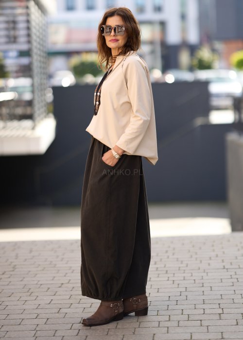 Brązowa spódnica maxi z elastyczną talią i kieszeniami, o luźnym kroju, zestawiona z beżową bluzką i brązowymi botkami w eleganckiej, miejskiej stylizacji.
