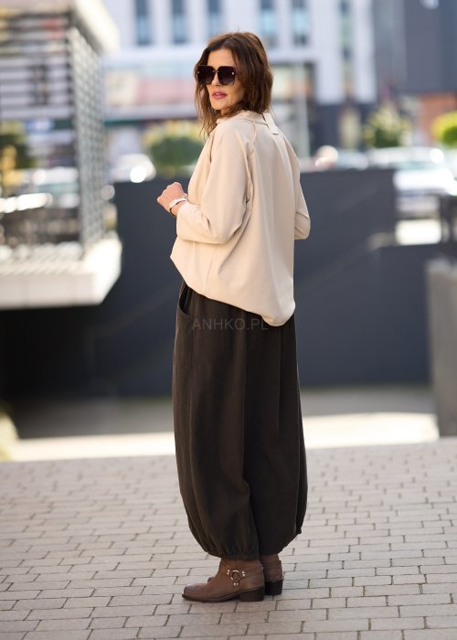 Brązowa spódnica maxi z elastyczną talią i kieszeniami, o luźnym kroju, zestawiona z beżową bluzką i brązowymi botkami w eleganckiej, miejskiej stylizacji.