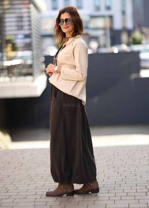 Brązowa spódnica maxi z elastyczną talią i kieszeniami, o luźnym kroju, zestawiona z beżową bluzką i brązowymi botkami w eleganckiej, miejskiej stylizacji.