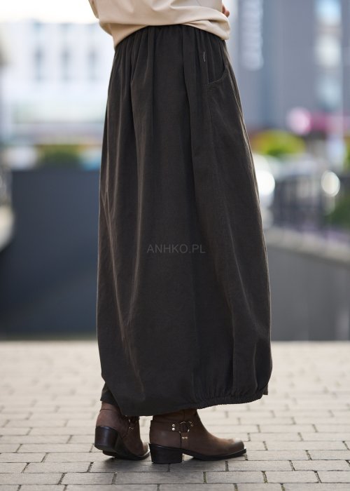 Brązowa spódnica maxi z elastyczną talią i kieszeniami, o luźnym kroju, zestawiona z beżową bluzką i brązowymi botkami w eleganckiej, miejskiej stylizacji.