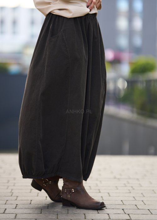 Brązowa spódnica maxi z elastyczną talią i kieszeniami, o luźnym kroju, zestawiona z beżową bluzką i brązowymi botkami w eleganckiej, miejskiej stylizacji.