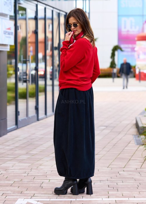 Czarna spódnica maxi z elastyczną talią i kieszeniami, o luźnym kroju, zestawiona z jasnym swetrem i czarnymi botkami na obcasie w miejskiej stylizacji.