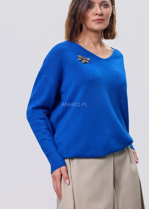 Kobaltowy sweter damski z miękkiej dzianiny, zintegrowany z długim szalem luźno opadającym przy dekolcie; model o swobodnym kroju, długi rękaw, stylizowany na jasnym tle
