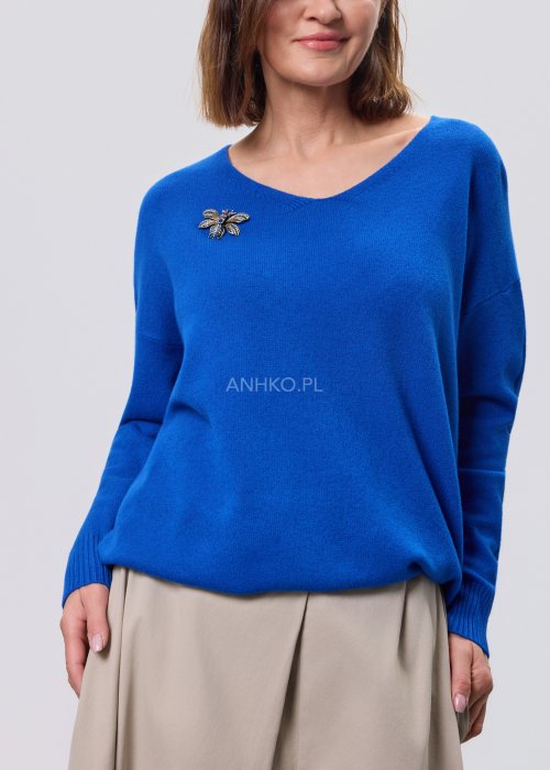 Kobaltowy sweter damski z miękkiej dzianiny, zintegrowany z długim szalem luźno opadającym przy dekolcie; model o swobodnym kroju, długi rękaw, stylizowany na jasnym tle