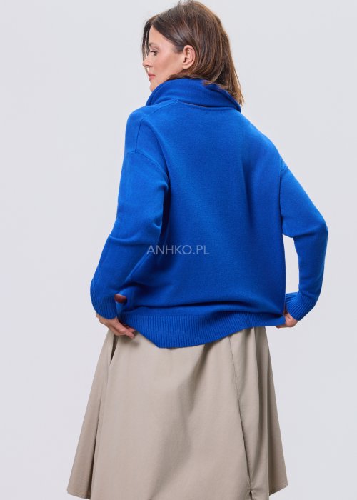 Kobaltowy sweter damski z miękkiej dzianiny, zintegrowany z długim szalem luźno opadającym przy dekolcie; model o swobodnym kroju, długi rękaw, stylizowany na jasnym tle