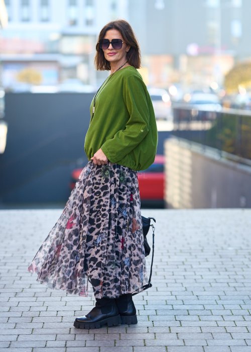 Zielona bluzka oversize z długim rękawem i regulowanym dołem, stylizowana z printowaną spódnicą maxi i botkami w miejskim looku.