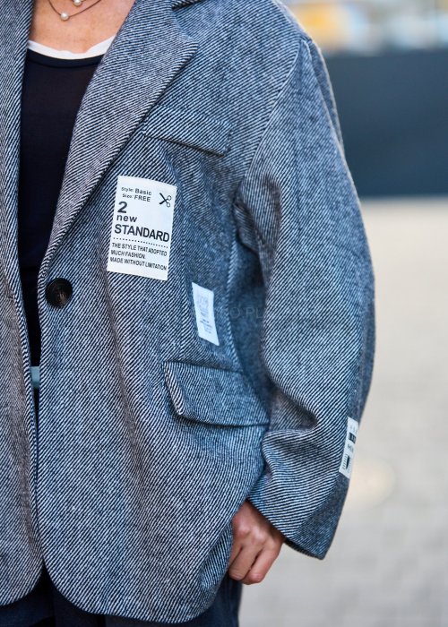 Szara marynarka damska w drobną jodełkę o kroju oversize z ozdobnymi naszywkami, stylizacja z czarnym topem i szerokimi spodniami.