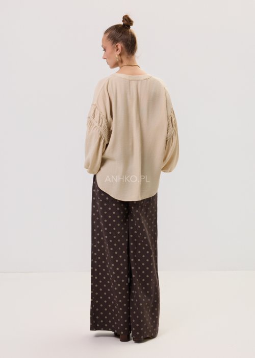 Brązowe damskie spodnie Retro Dots z szeroką nogawką, ozdobione beżowymi groszkami. Model z wysokim stanem i paskiem w talii, w stylizacji z kremowym topem oraz brązowymi botkami.
