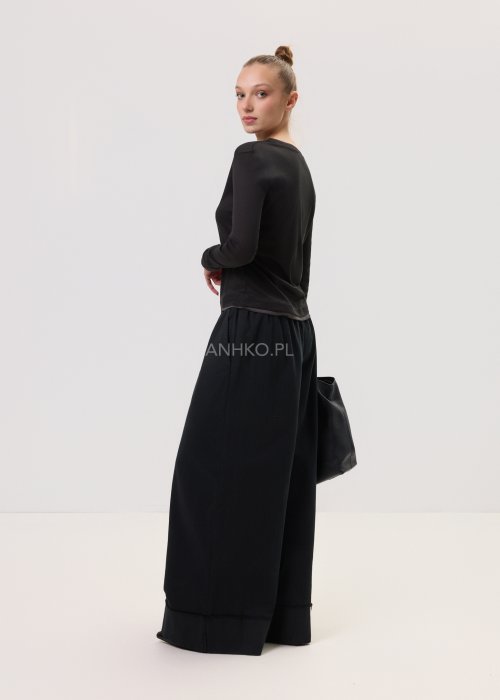 Czarna bluzka damska z długim rękawem o prostym, minimalistycznym kroju, zestawiona z szerokimi czarnymi spodniami w eleganckiej stylizacji.