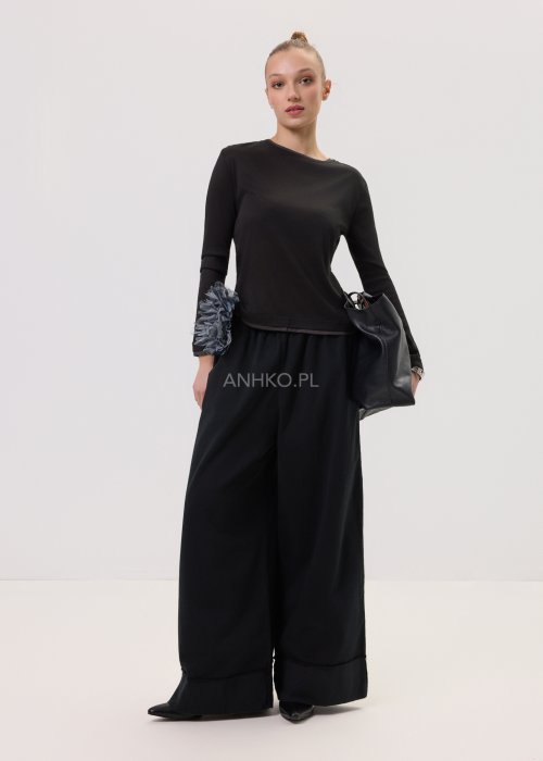 Czarna bluzka damska z długim rękawem o prostym, minimalistycznym kroju, zestawiona z szerokimi czarnymi spodniami w eleganckiej stylizacji.