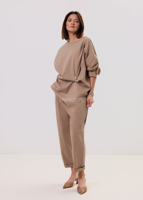 Spodnie Starola Rose Cappuccino w odcieniu ciepłego beżu, z podwiniętą nogawką i eleganckim paskiem, w minimalistycznej stylizacji z butami na obcasie.