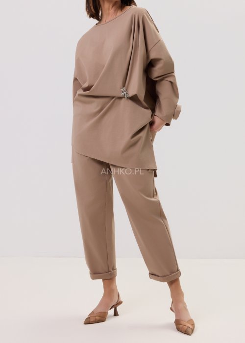 Spodnie Starola Rose Cappuccino w odcieniu ciepłego beżu, z podwiniętą nogawką i eleganckim paskiem, w minimalistycznej stylizacji z butami na obcasie.