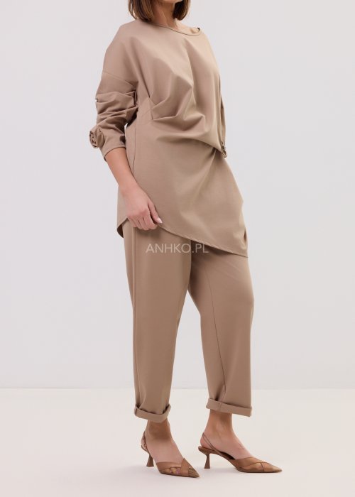 Spodnie Starola Rose Cappuccino w odcieniu ciepłego beżu, z podwiniętą nogawką i eleganckim paskiem, w minimalistycznej stylizacji z butami na obcasie.