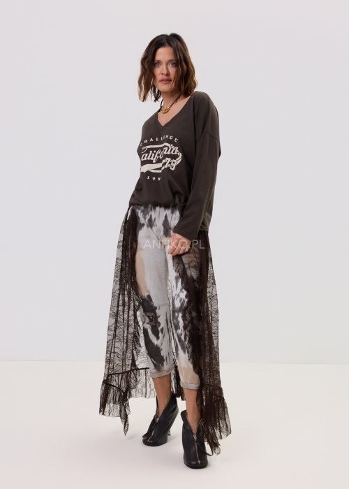 Brązowa bluzka oversize z długim rękawem i dekoltem V, z nadrukiem „California 79”, zestawiona z jeansami tie-dye i koronkową narzutką w stylizacji casua