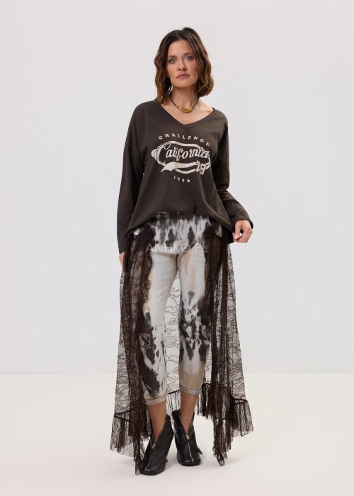 Brązowa bluzka oversize z długim rękawem i dekoltem V, z nadrukiem „California 79”, zestawiona z jeansami tie-dye i koronkową narzutką w stylizacji casual