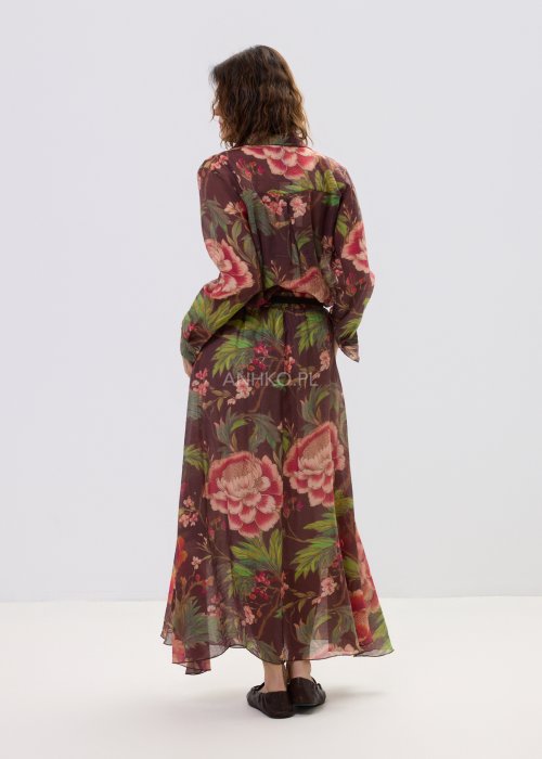 Zwiewna spódnica maxi w kwiatowy wzór na ciemnym tle z dekoracyjnym paskiem i kwiatową aplikacją. Lekka, elegancka spódnica damska z romantycznym printem, idealna do stylizacji boho i casual chic.