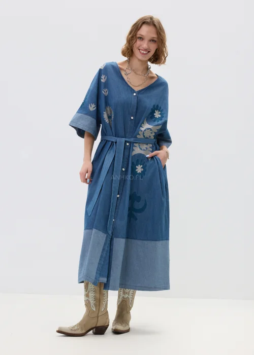 Jeansowa sukienka maxi w odcieniu niebieskiego denimu z haftowanymi wzorami, wiązana w talii paskiem, zapinana na guziki, o luźnym fasonie z szerokimi rękawami, stylizowana z kowbojkami.