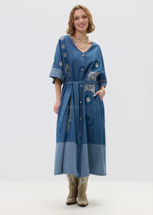 Jeansowa sukienka maxi w odcieniu niebieskiego denimu z haftowanymi wzorami, wiązana w talii paskiem, zapinana na guziki, o luźnym fasonie z szerokimi rękawami, stylizowana z kowbojkami.